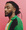 Ein Mann mit Dreadlocks trägt eine bunte, gehäkelte Jacke vor einem pinken Hintergrund.