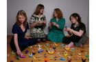 Download Foto: Vier Frauen sitzen auf dem Boden, umgeben von bunten Origami-Figuren, und falten Papierkreaturen.