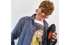 Download Foto: Person mit brauner Perücke und Sonnenbrille hält eine Schallplatte. Sie trägt ein bedrucktes T-Shirt und ein offenes Hemd.