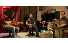Download Foto: Drei Musiker in einem Raum: Einer spielt E-Gitarre, der zweite Bass und der dritte Schlagzeug. Hintergrund mit rotem Vorhang.