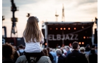 Download Foto: Ein Kind sitzt auf den Schultern einer Person und blickt auf eine Bühne mit dem Schriftzug 'ELBJAZZ'. Im Hintergrund sind Kräne zu sehen.