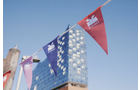 Download Foto: Bunte Wimpel vor einem modernen Gebäude mit Glasfassade unter blauem Himmel.