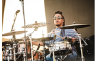 Download Foto: Eine Person spielt Schlagzeug auf einer Bühne, trägt eine Sonnenbrille und hat Dreadlocks. Im Hintergrund befindet sich ein Mikrofon.