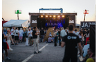 Download Foto: Menschenmenge vor einer Bühne bei Abenddämmerung auf einem Open-Air-Festival. Bühne beleuchtet, 'JAZZ' sichtbar.