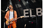 Download Foto: Ein Musiker in orangener Kleidung spielt E-Gitarre und singt auf einer Bühne vor einem schwarzen Hintergrund mit der Aufschrift 'ELB'.