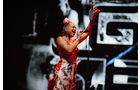 Download Foto: Sängerin in rotem Kleid singt leidenschaftlich auf der Bühne, hält Mikrofon, Hintergrund unscharf mit schwarz-weißen Mustern.