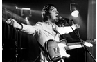 Download Foto: Musiker auf der Bühne, spielt E-Gitarre und singt leidenschaftlich ins Mikrofon, Arme ausgebreitet, Schwarz-Weiß-Foto.