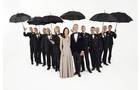 Download Foto: Eine Frau in einem Abendkleid und ein Mann im Smoking stehen vor einer Gruppe von Männern mit Regenschirmen, die sie umrahmen.