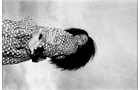 Download Foto: Eine Person in einem gemusterten Kleid steht mit ausgestreckten Armen seitlich. Der Hintergrund ist wolkig. Schwarzweiß-Fotografie.