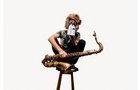 Download Foto: Person sitzt auf Hocker, hält ein Saxophon, trägt Blumenkranz und verdeckt das Gesicht mit einem Milchkarton. Hintergrund ist weiß.