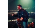 Download Foto: Ein Sänger performt leidenschaftlich auf der Bühne vor einem großen, erleuchteten Publikum in einem Konzertsaal.