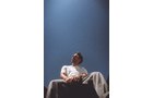 Download Foto: Eine Person in weißem T-Shirt sitzt vor einem blauen Himmel, von unten fotografiert, mit entspanntem Gesichtsausdruck.
