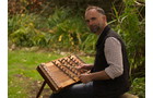 Download Foto: Ein Mann spielt ein traditionelles Musikinstrument in einem grünen Garten.