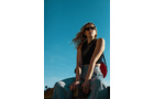 Download Foto: Frau mit Sonnenbrille sitzt entspannt unter blauem Himmel. Sie trägt ein schwarzes Top und helle Jeans.