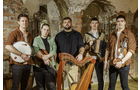 Download Foto: Fünf Personen mit traditionellen Instrumenten posieren vor einer rustikalen Wand. Sie halten Harfe, Geige, und andere Instrumente.