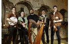 Download Foto: Fünf Männer stehen in einem rustikalen Raum, halten traditionelle Musikinstrumente wie Tamburin, Harfe und Geige.