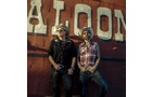 Download Foto: Zwei Personen in Cowboykleidung stehen vor einer roten Wand mit dem Schriftzug 'SALON'.