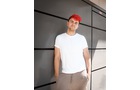 Download Foto: Eine Person mit roter Kappe und weißem T-Shirt lehnt an einer grauen Wand.