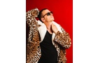 Download Foto: Person in Leopardenmantel und Sonnenbrille vor rotem Hintergrund, blickt nach oben.
