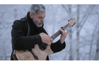 Download Foto: Ein Mann mit grauem Haar spielt im Freien eine Akustikgitarre, umgeben von schneebedeckten Bäumen.