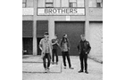 Download Foto: Vier Personen stehen vor einem Gebäude mit dem Schriftzug 'Brothers', schwarz-weiß Bild, lässige Kleidung und entspannte Haltung.