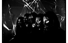 Download Foto: Fünf Personen stehen in einem dunklen Raum, beleuchtet durch diagonale Lichtstreifen, die ihre Gesichter teils im Schatten lassen.