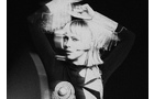 Download Foto: Schwarz-weiß-Foto einer Person mit blondem Bob, die die Arme über dem Kopf hält, in futuristischem Outfit mit geometrischen Formen.