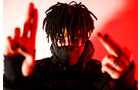 Download Foto: Eine Person mit dunklen Dreadlocks und Maske hält ihre Hände gestikulierend vor sich. Der Hintergrund ist rot beleuchtet.