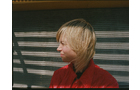 Download Foto: Person mit blondem Haar und rotem Hemd im Profil vor einer Wand mit Schattenstreifen.