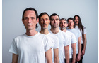 Download Foto: Sechs Männer stehen in einer diagonalen Linie, alle tragen weiße T-Shirts und schauen ernst in die Kamera.
