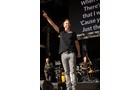 Download Foto: Musiker auf der Bühne, hält das Mikrofon und zeigt mit der anderen Hand nach oben. Im Hintergrund eine Band und ein Bildschirm mit Songtexten.
