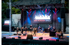 Download Foto: Eine Bühnenperformance mit Musikern vor einem beleuchteten Hintergrund. Der Schriftzug 'DER NORDEN SINGT' ist sichtbar.