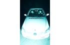 Download Foto: Ansicht eines weißen Autos mit sichtbarer Vorderseite in hellem Licht, auf einer dunklen Straße geparkt.