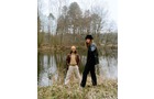 Download Foto: Zwei Personen stehen vor einem Teich im Freien, umgeben von Bäumen. Eine Person trägt einen schwarzen Mantel, die andere einen gelben Hut.