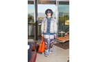 Download Foto: Person in bunter, gemusterter Kleidung und großer Sonnenbrille steht mit orangefarbener Tasche in modernem Raum vor Glasfront.