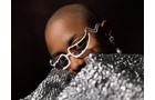 Download Foto: Person mit Glitzerbrille und glänzendem, silbernem Outfit, schaut über die Schulter. Hintergrund dunkel.