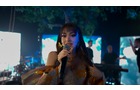 Download Foto: Eine Sängerin performt auf einer Bühne mit bunten Lichtern und Musikern im Hintergrund. Sie hält ein Mikrofon in der Hand.