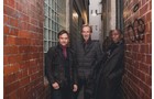 Download Foto: Drei Personen in Winterkleidung stehen in einer schmalen Gasse zwischen roten Backsteinwänden und Glasbausteinen.