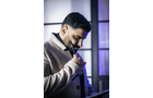 Download Foto: Ein Mann in einem hellen Mantel steht nachdenklich mit einem Tablet und einem Stift in der Hand vor einem Fenster mit blauem Licht.