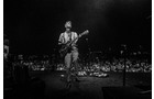 Download Foto: Ein Musiker spielt Gitarre auf einer Bühne vor einem großen Publikum. Die Szene ist in Schwarz-Weiß gehalten.