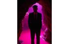 Download Foto: Eine Silhouette einer Person in einem Anzug steht in einem Höhleneingang, beleuchtet von pinkem Licht.