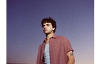 Download Foto: Junger Mann in rotem Hemd und blauem Shirt steht vor wolkenlosem, violettem Himmel, schaut in die Ferne.