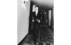 Download Foto: Eine Person in einem eleganten Anzug geht einen langen Flur entlang, der mit einem gemusterten Teppich ausgelegt ist. Schwarz-Weiß-Foto.
