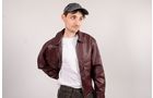 Download Foto: Eine Person trägt eine braune Lederjacke, ein weißes T-Shirt und eine graue Baseballkappe und blickt zur Seite.