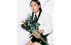Download Foto: Person mit dunklem Haar und Hemd hält rote Rosen und Eukalyptus, während sie auf einem weißen Bett liegt und in die Kamera schaut.