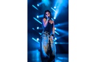 Download Foto: Eine Sängerin performt auf der Bühne in schicker Beleuchtung. Sie trägt ein schwarzes Oberteil und weite Jeans.