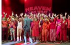 Download Foto: Eine Gruppe von Menschen in roten und pinken Outfits hebt auf einer Bühne die Arme, im Hintergrund steht Heaven Can Wait.