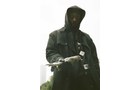 Download Foto: Eine Person in dunkler Kleidung mit Kapuze hält eine Kamera und blickt ernst in die Kamera. Der Hintergrund ist hell.