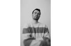 Download Foto: Ein Mann mit kurzem Haar trägt einen gestreiften Pullover. Das Bild ist schwarz-weiß und leicht verschwommen, mit neutralem Hintergrund.