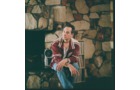 Download Foto: Eine Person in Jeans und kariertem Hemd sitzt in einem Raum mit einer Wand aus Naturstein.